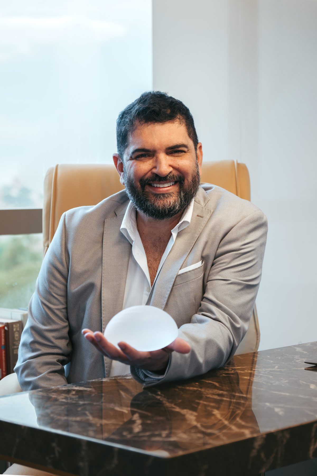 Dr. Charles Farias no consultório segurando uma prótese mamária